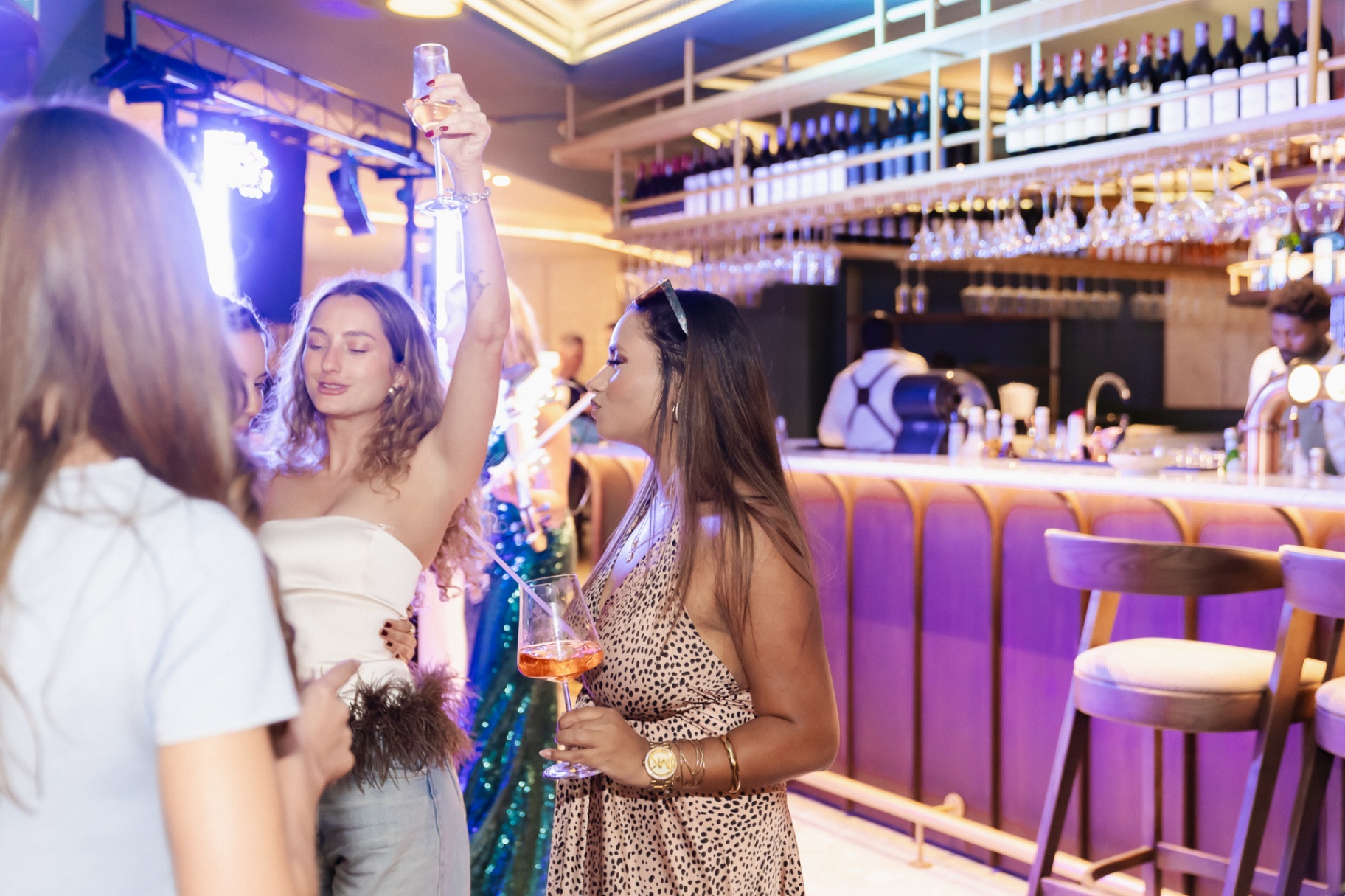 Friends with drinks at the Noah bar under purple lighting on First Thursdays