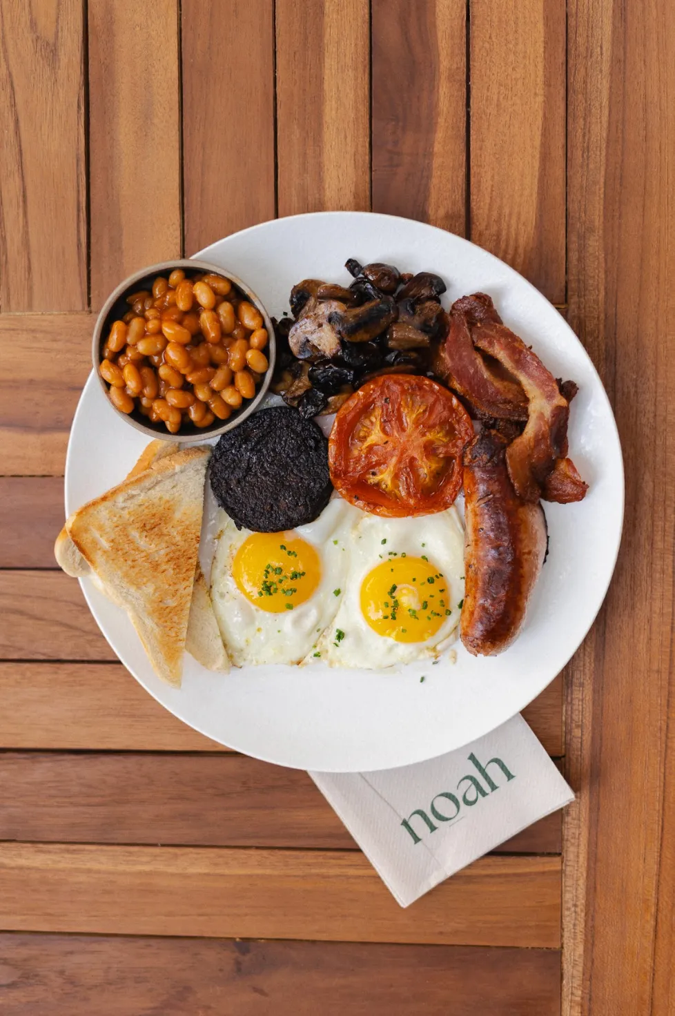 Full English breakfast plate with bacon, eggs, sausage and sourdough at Noah Cape Town